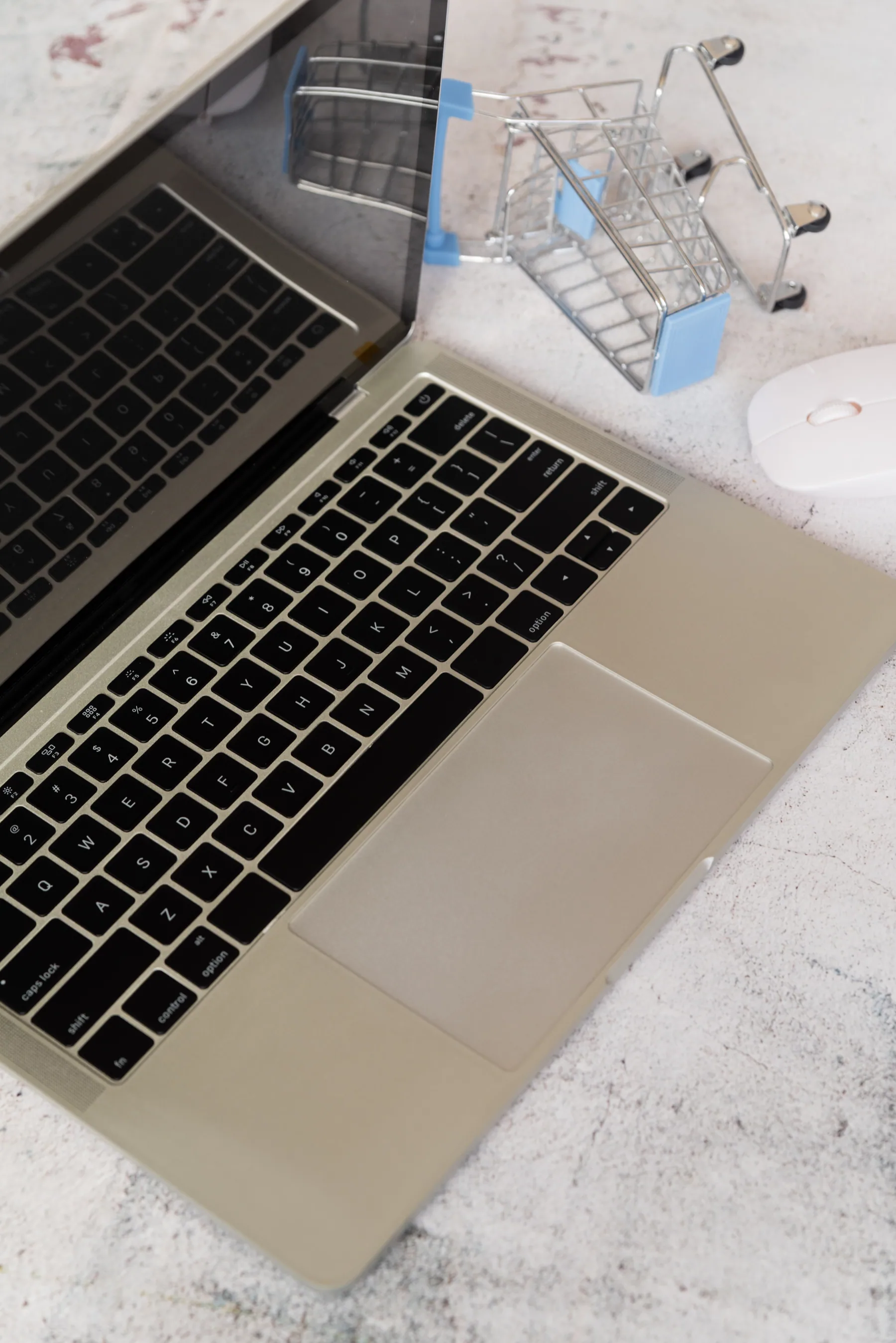 A miniature shopping trolley resting on an open laptop