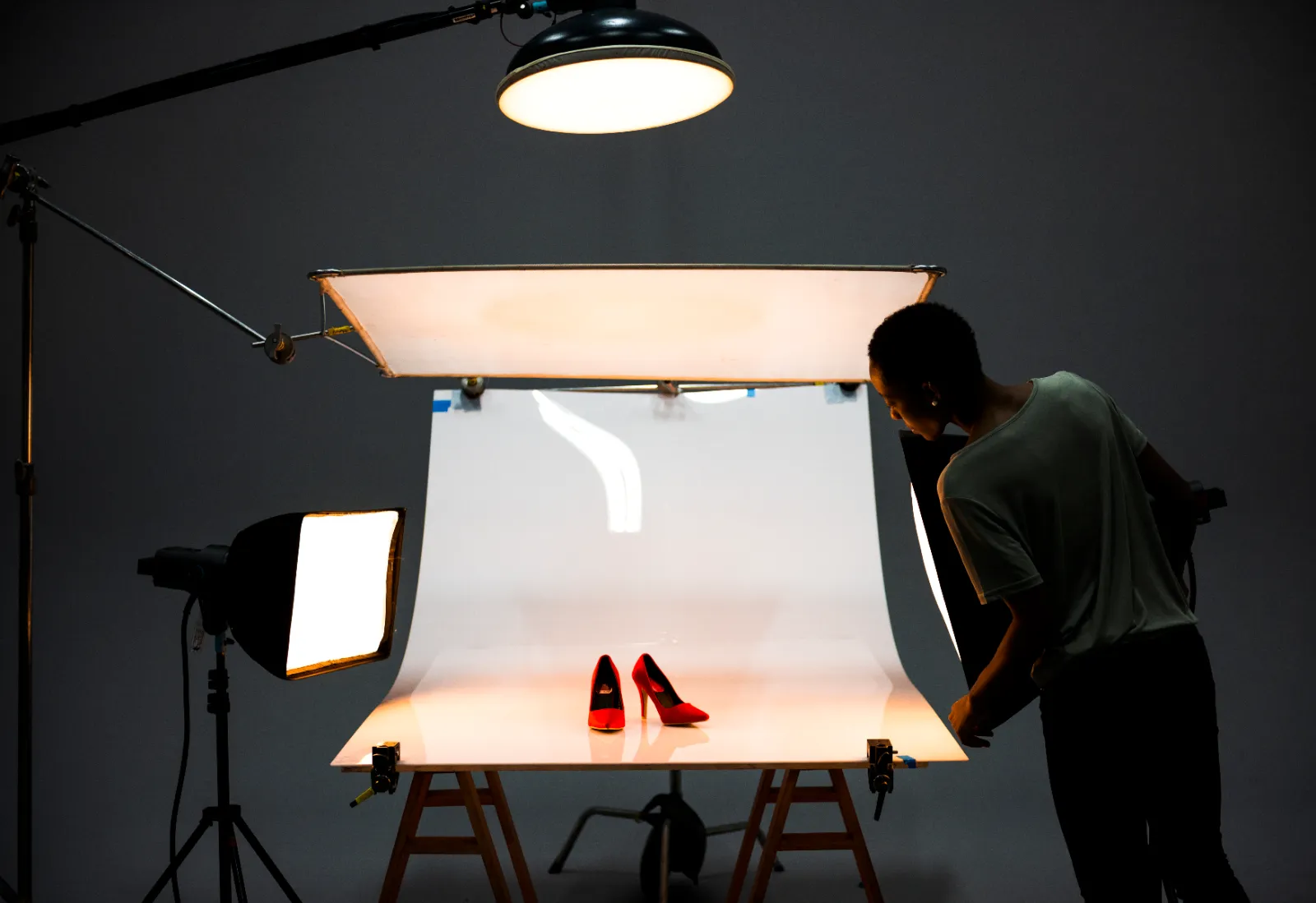 A photographer shooting a pair of red heels on a lit white sweep in a studio