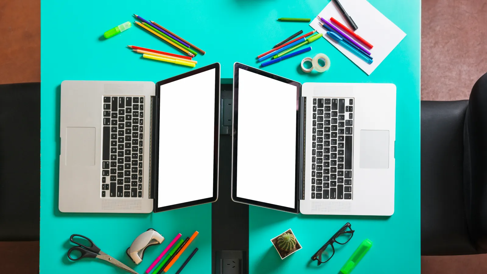 Two near-identical open laptops facing each other on a turquoise desk