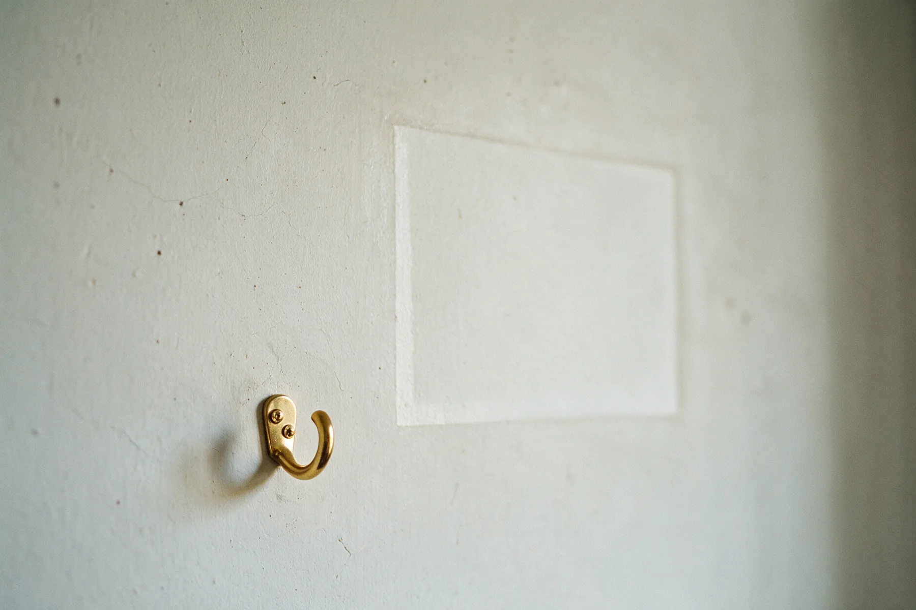 An empty brass picture hook on a pale wall, with the faded rectangle where a framed print used to hang