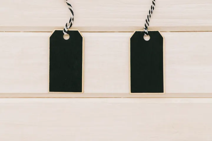 Two blank black price tags hanging side by side against pale wood