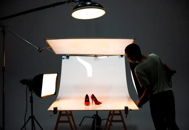 A photographer shooting a pair of red heels on a lit white sweep in a studio