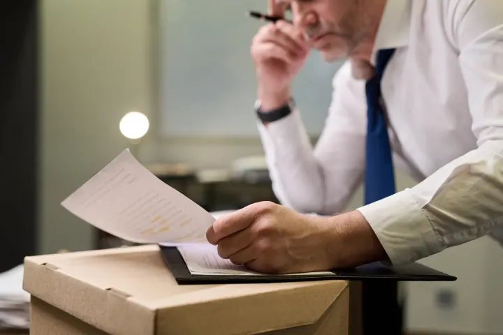 Reading a document at a desk beside an opened shipping box