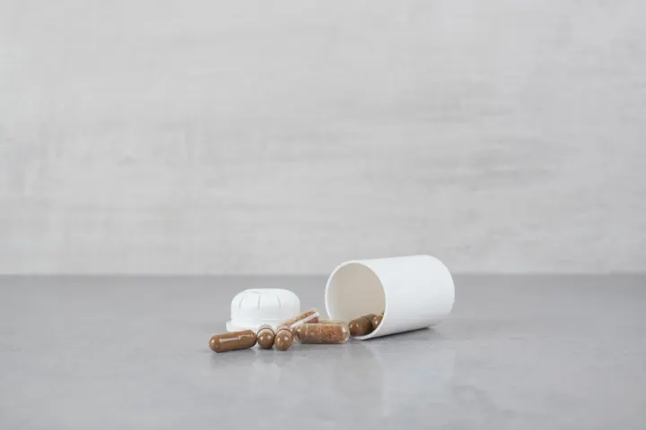 A white supplement bottle tipped over on a grey surface with capsules spilling out