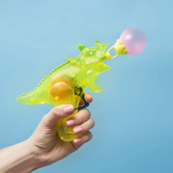 A novelty dinosaur bubble gun held against a blue background