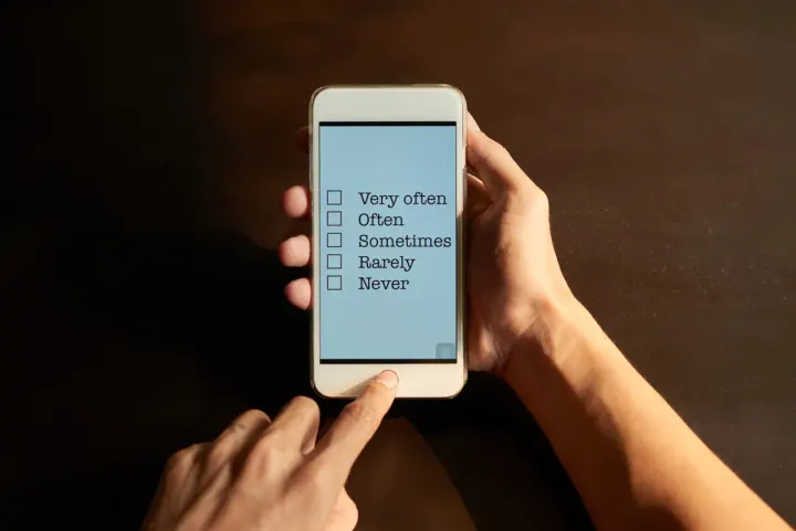 Hands tapping a survey rating scale on a phone in a dark room