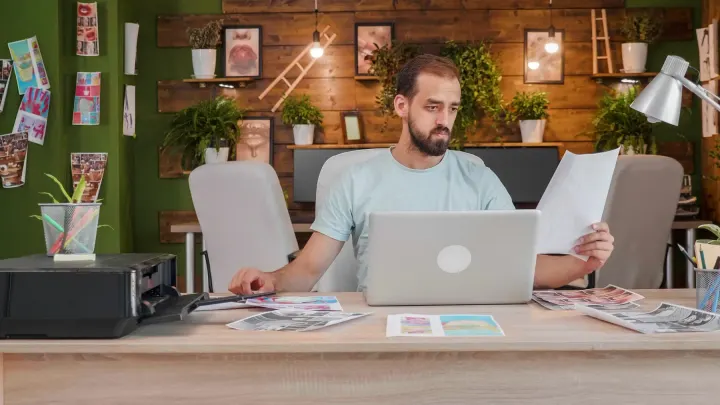 A designer at a studio desk reviewing printed layouts